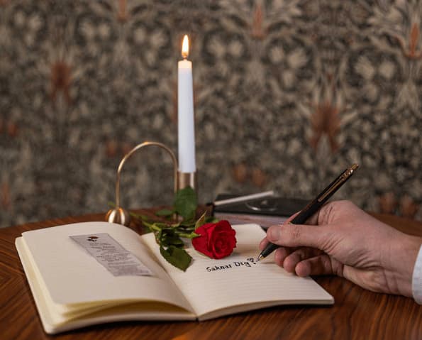 Ett ljus, en ros och någon som skriver "saknar dig" i en bok.