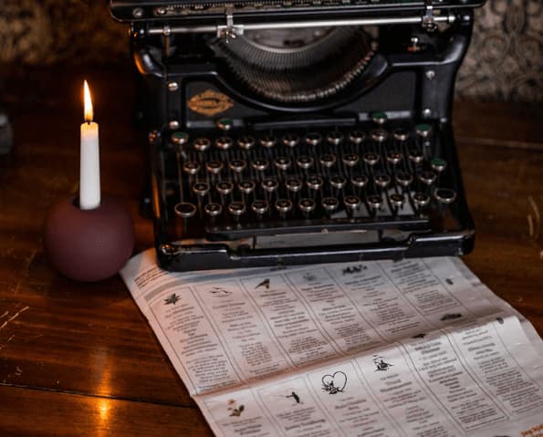 Gammalskrivmaskin på bord med ljus och dödsannonser i tidning